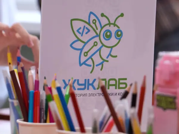Табличка ЖукЛаба и стаканчики с карандашами на столе мастер-класса